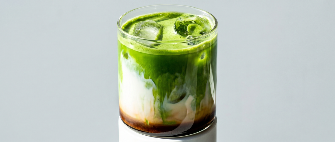 Dirty matcha latte in a clear glass — matcha green layer over milk with an espresso shot poured on top, served over ice