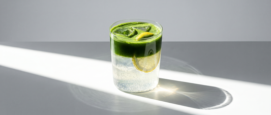 Iced matcha lemonade in a tall glass — bright green matcha floating over sparkling lemonade, garnished with a lemon slice and ice