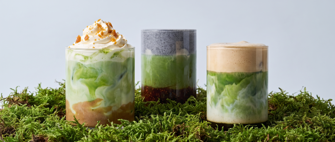 Three autumn matcha drinks with chestnut, black sesame and fig, and brown sugar hojicha cream, arranged in fresh green moss against a soft grey-blue background.