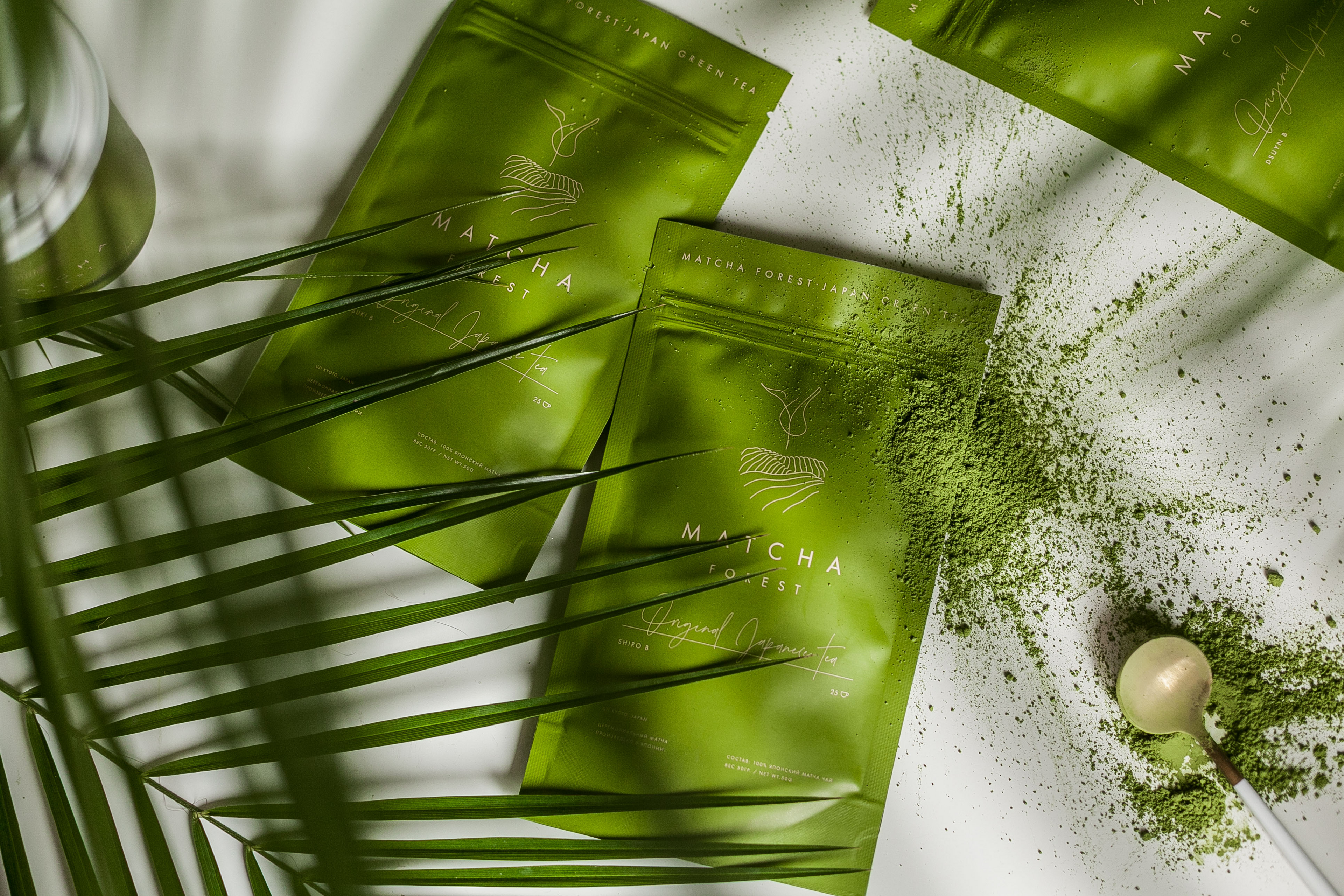 Matcha Forest Original Japanese Tea packs lying on scattered green matcha powder with a bamboo scoop