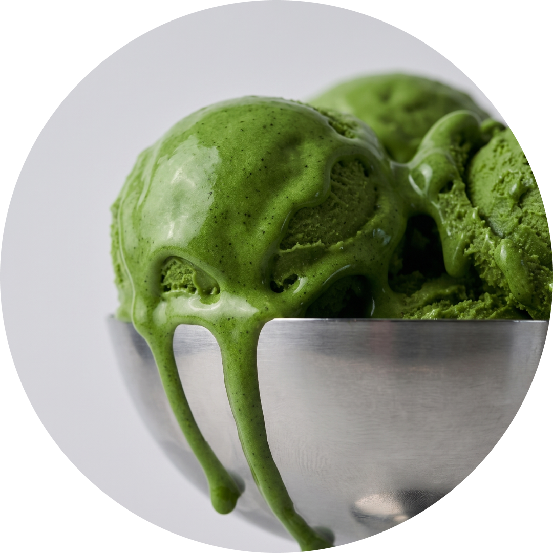 Matcha ice cream scoops with a glossy drizzle, dripping over the edge of a metal bowl against a light gray background.