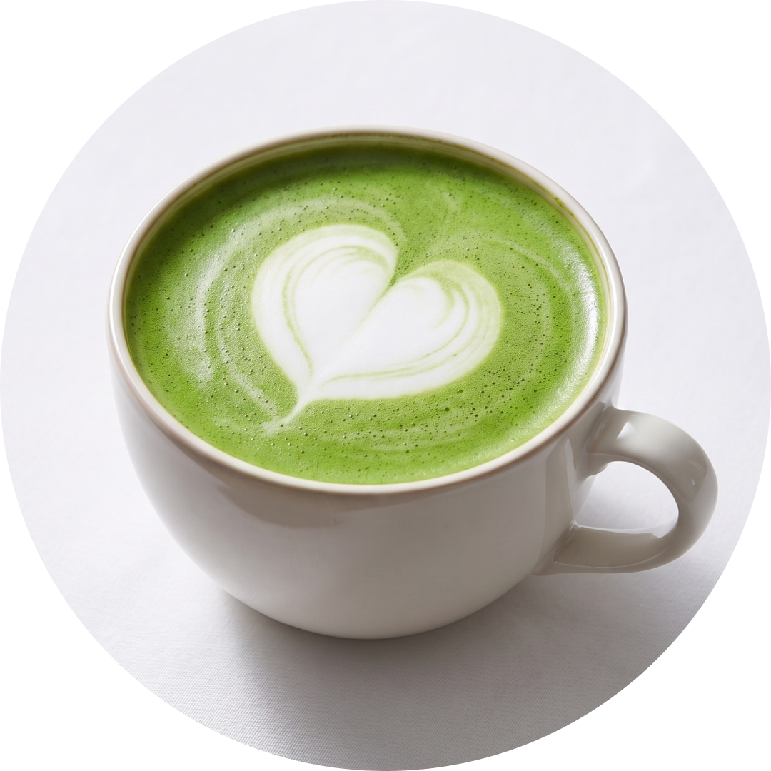 A white ceramic cup filled with a green matcha latte featuring a heart-shaped latte art, set against a clean white background.